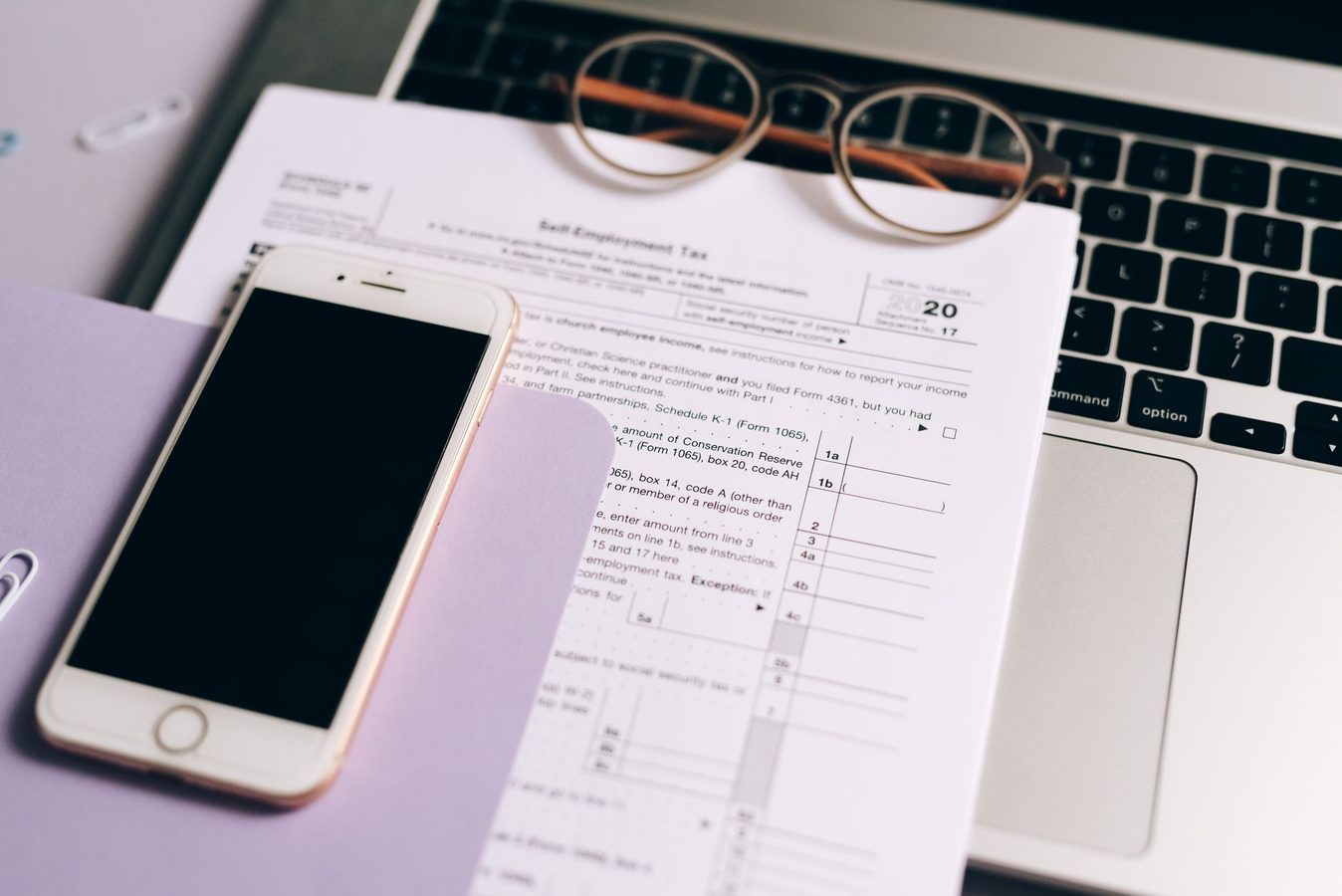 Federal tax forms beside a laptop on a kitchen table while someone looks up a refund status